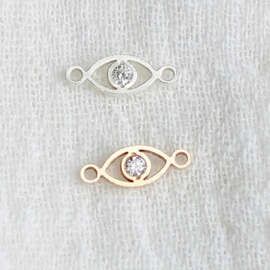 Two gold eye-shaped jewelry pieces with embedded stones on a light gray background